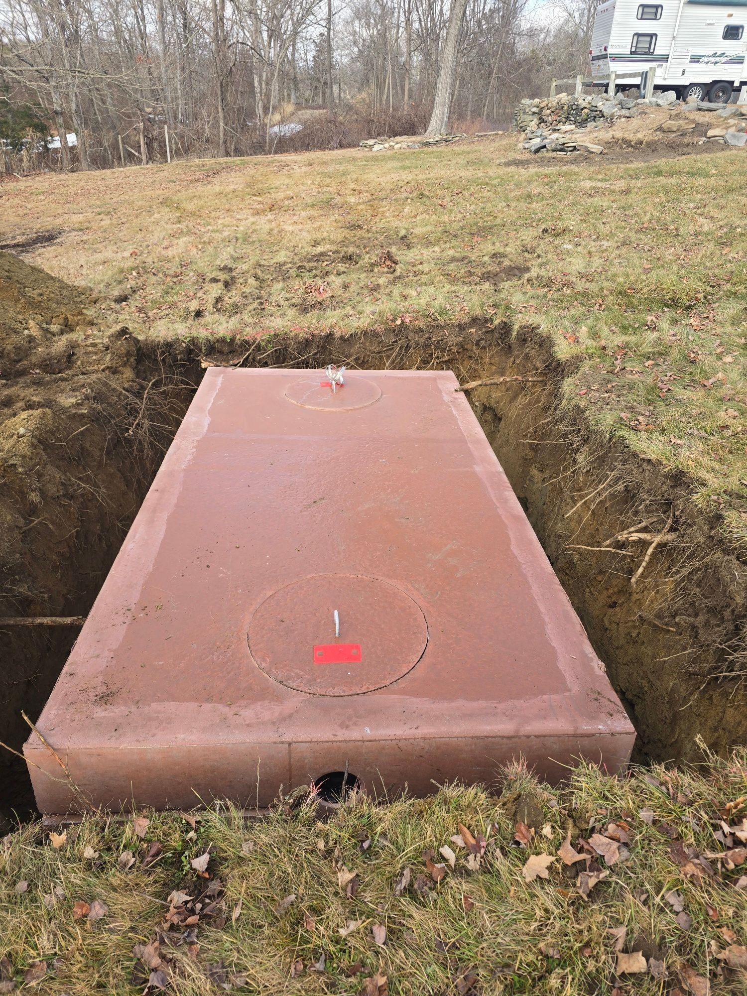 Brown rectangular septic tank in an excavated ditch, outdoors.
