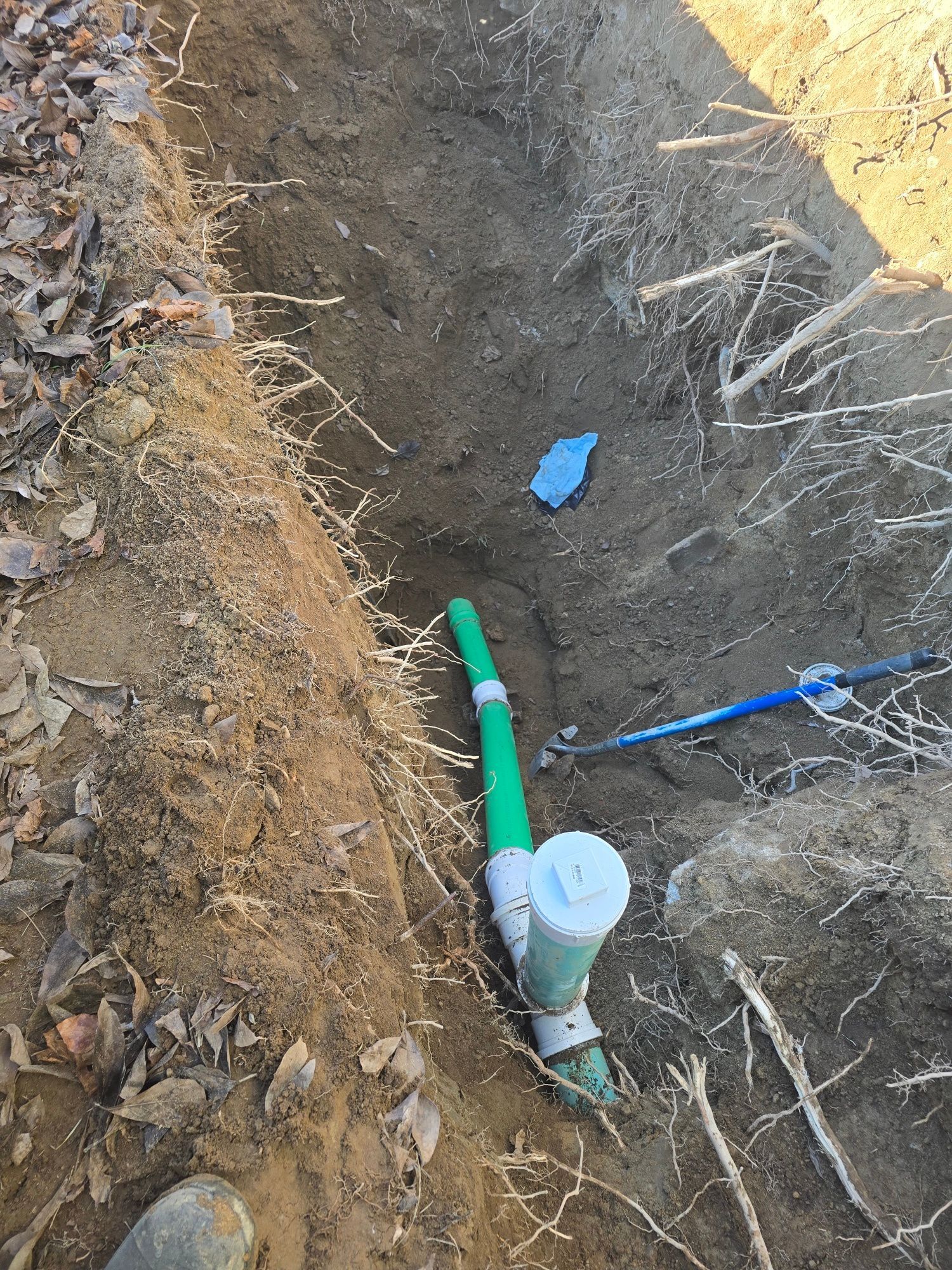 Trench with green pipe, a white cap, and blue object; soil and vegetation.