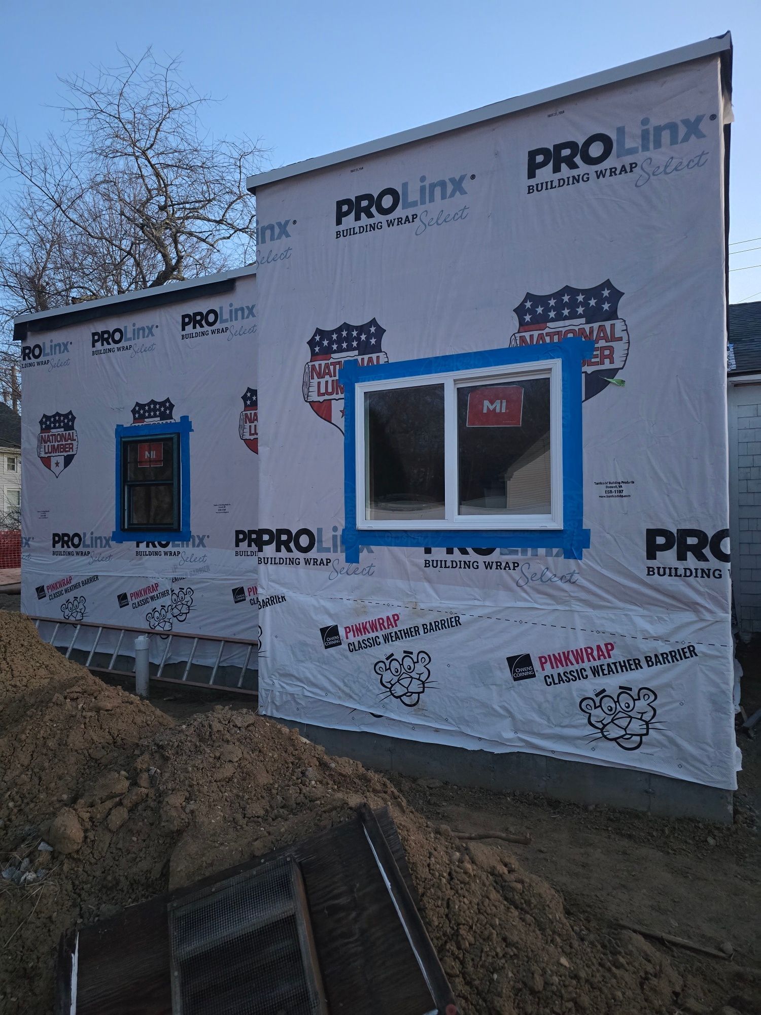 Exterior of a building under construction, wrapped in protective material, windows taped with blue.