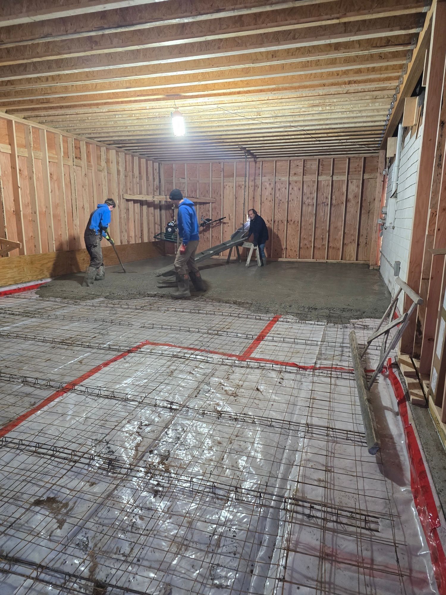 Three people are smoothing concrete in a room with wood framing and a wire mesh underlayment.