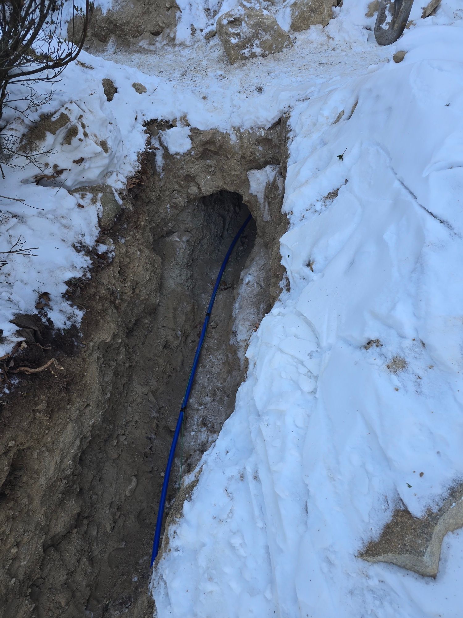 A trench in snowy ground with a blue cable running through it.