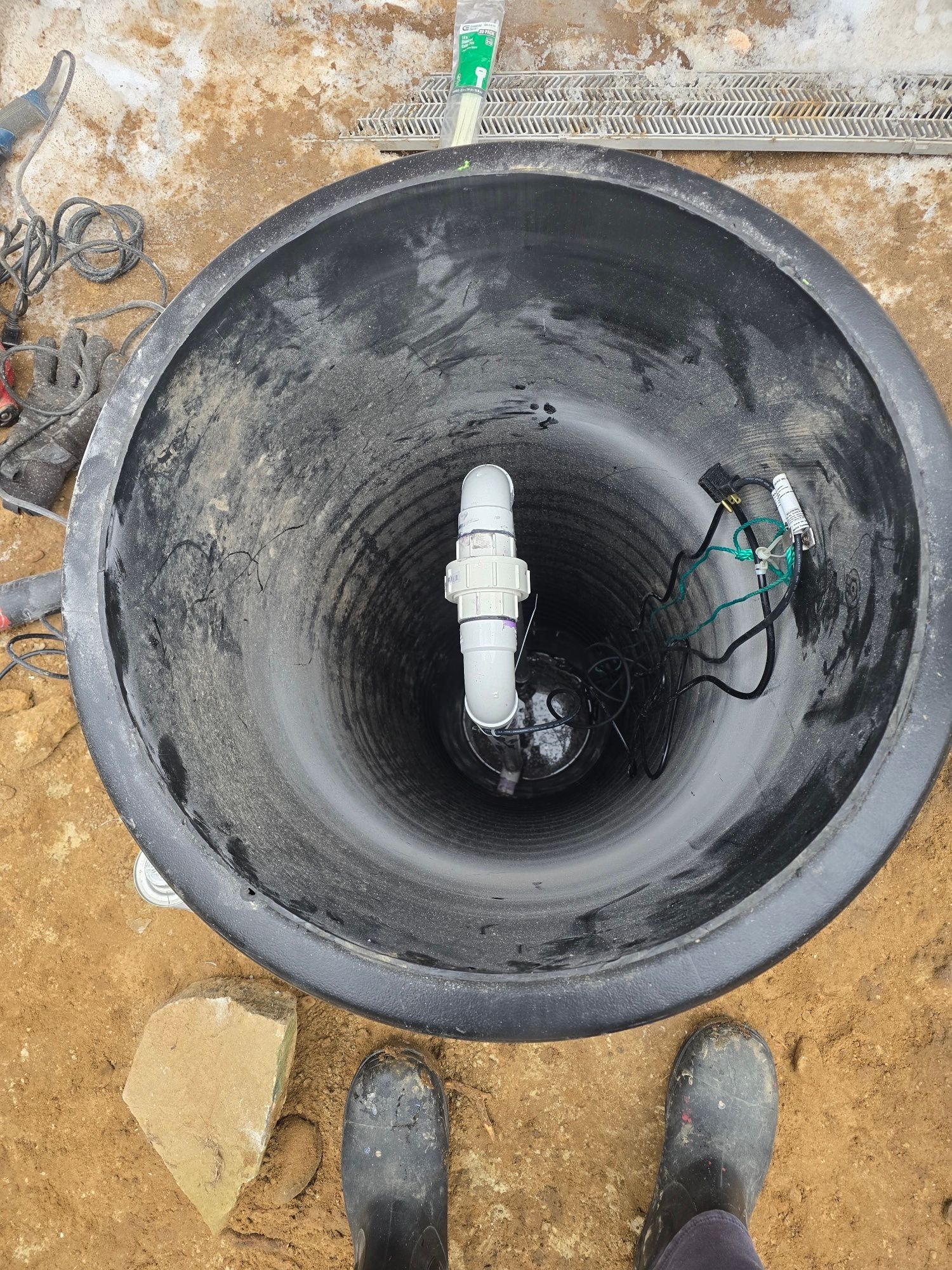 Overhead view of a deep, black, conical container. A white pipe is centered inside. Dirty work setting.