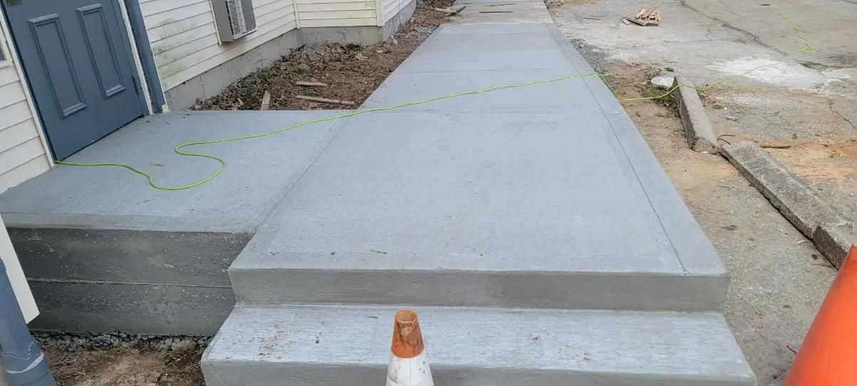 Newly poured concrete sidewalk and steps leading up to a building entrance.