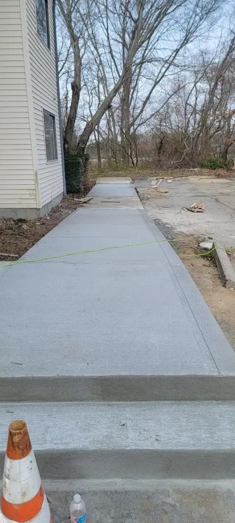 Concrete walkway and steps next to a building, orange traffic cone in foreground, trees in background.