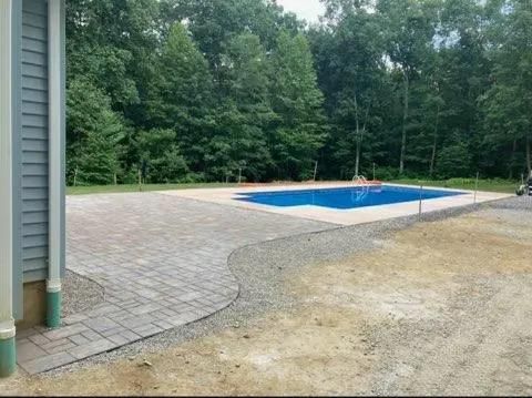 A backyard with a rectangular pool, surrounded by a brick patio and gravel. 