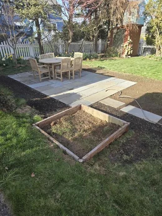 Backyard patio with wooden furniture, raised garden bed, and stone pathway.