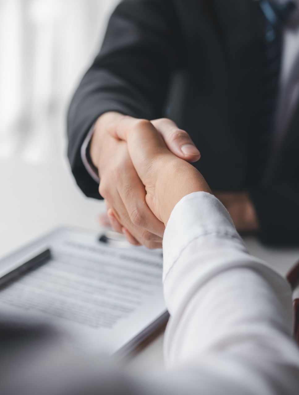 Two people shaking hands over a contract at a table.