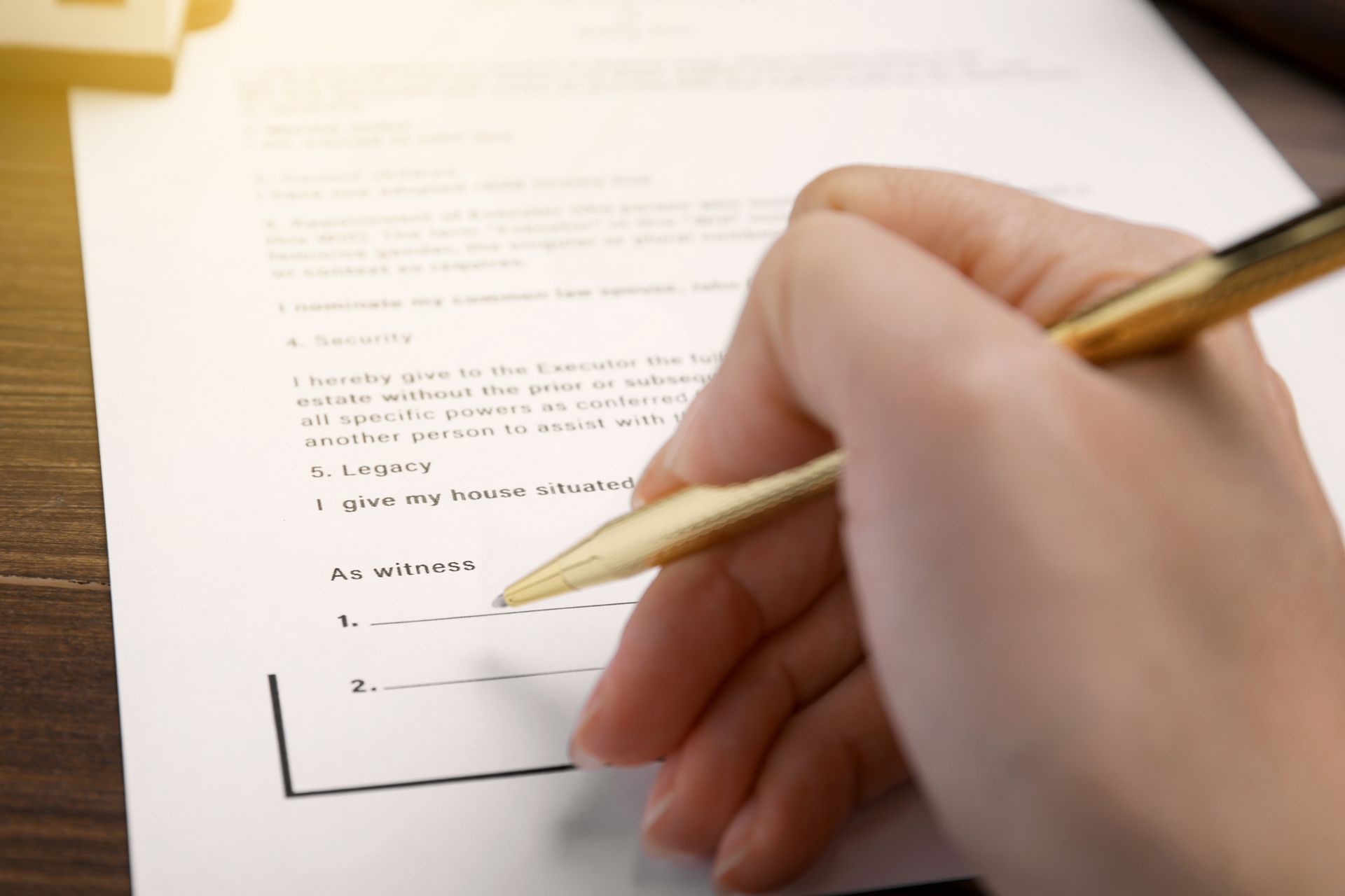 Hand holding gold pen, writing on a document with a signature line.