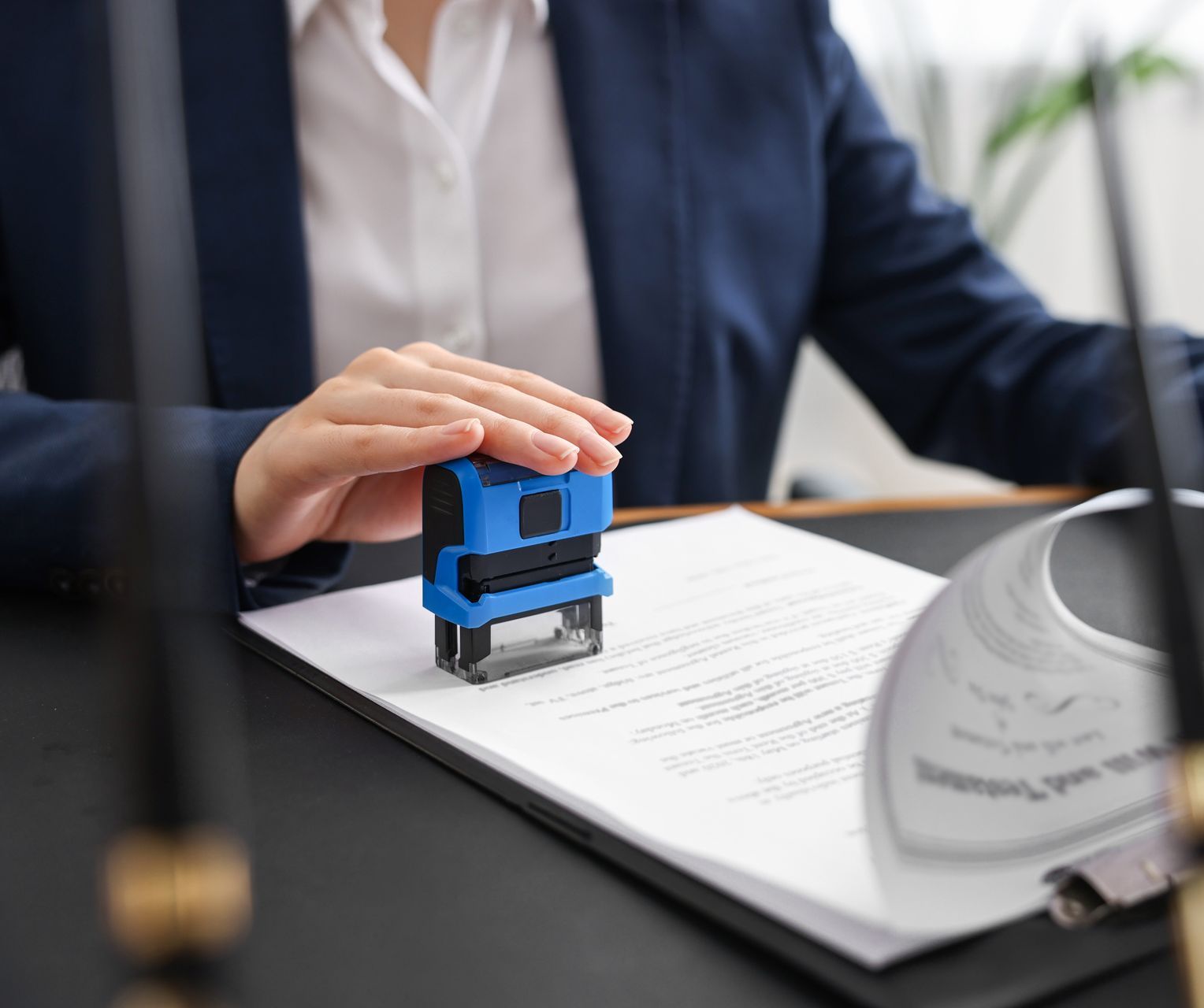 Person in suit stamps a document with a blue stamp at a desk.