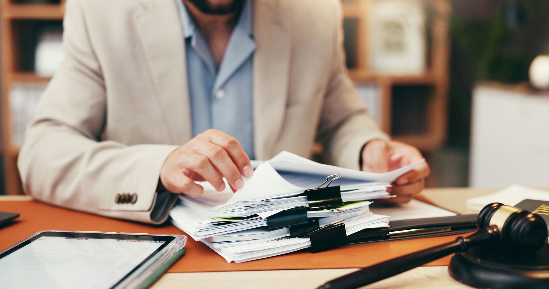 Man in suit reviewing a stack of documents with a gavel on the table.