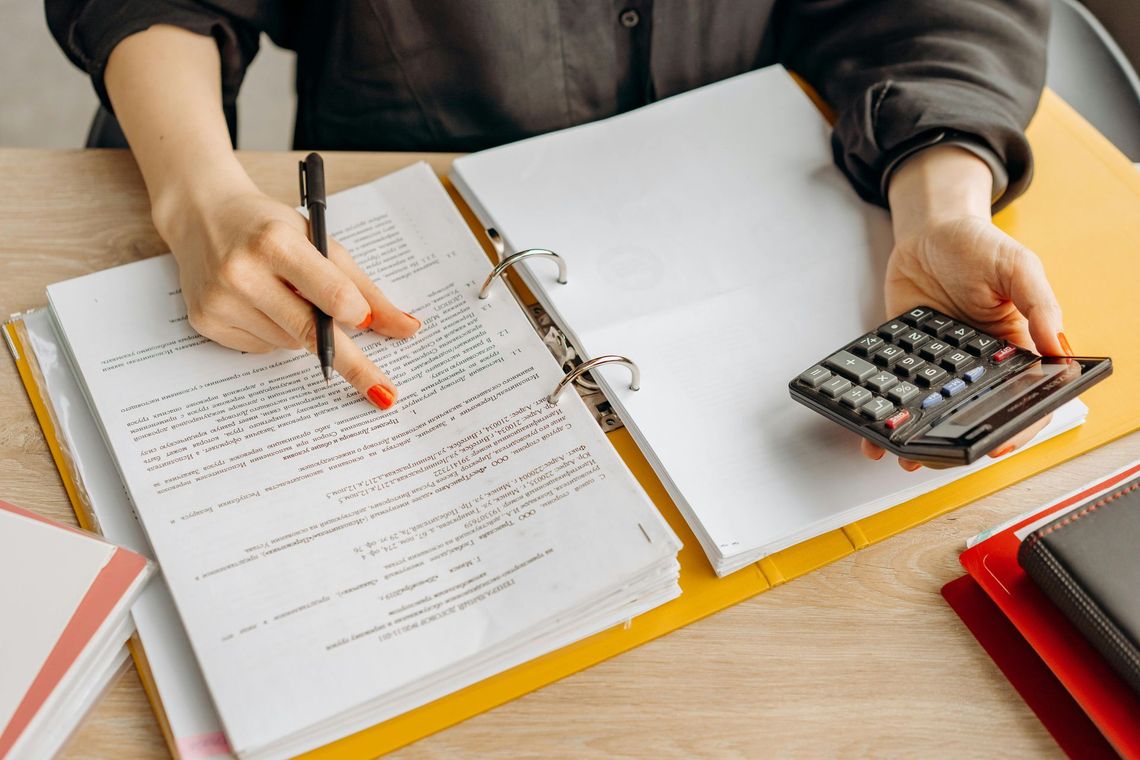 Hands pointing at paperwork and a calculator on a desk during bookkeeping review