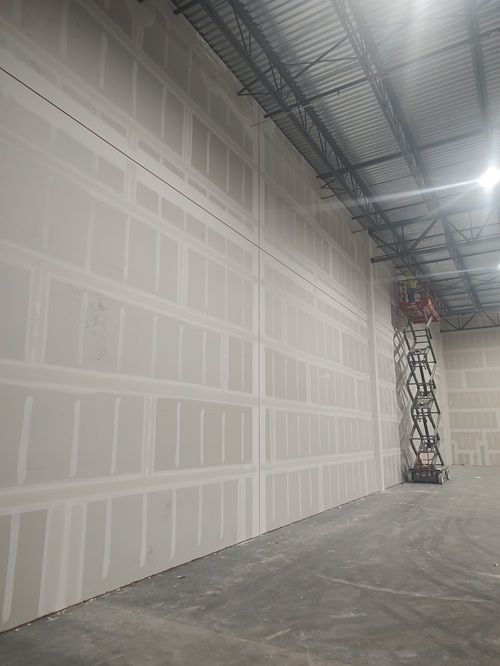 A man is standing on a ladder in a large warehouse with a large wall.