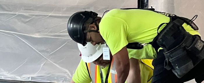 Two construction workers wearing hard hats and safety vests are working on a project.