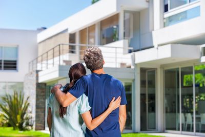 Two people embracing outside a modern white house with large windows and glass doors