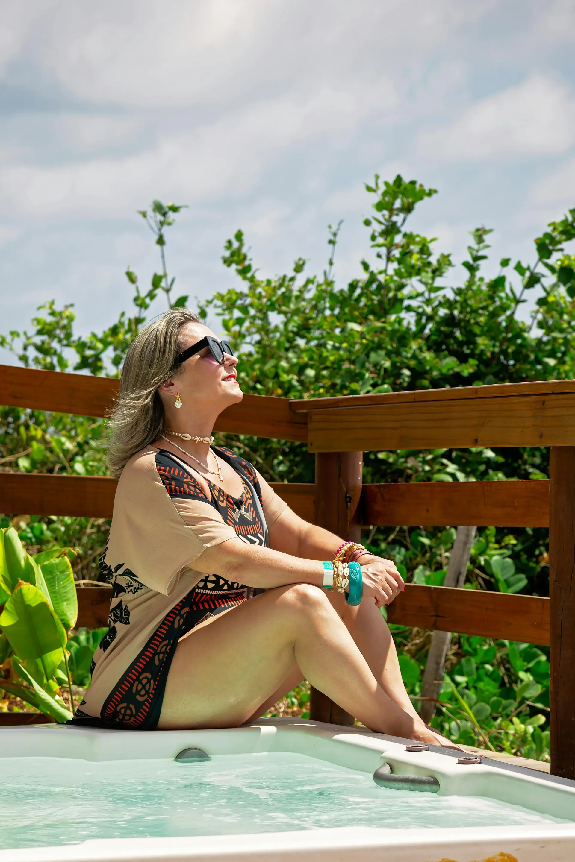 A women wearing sunglasses, sunny day sitting next to a jacuzzi.