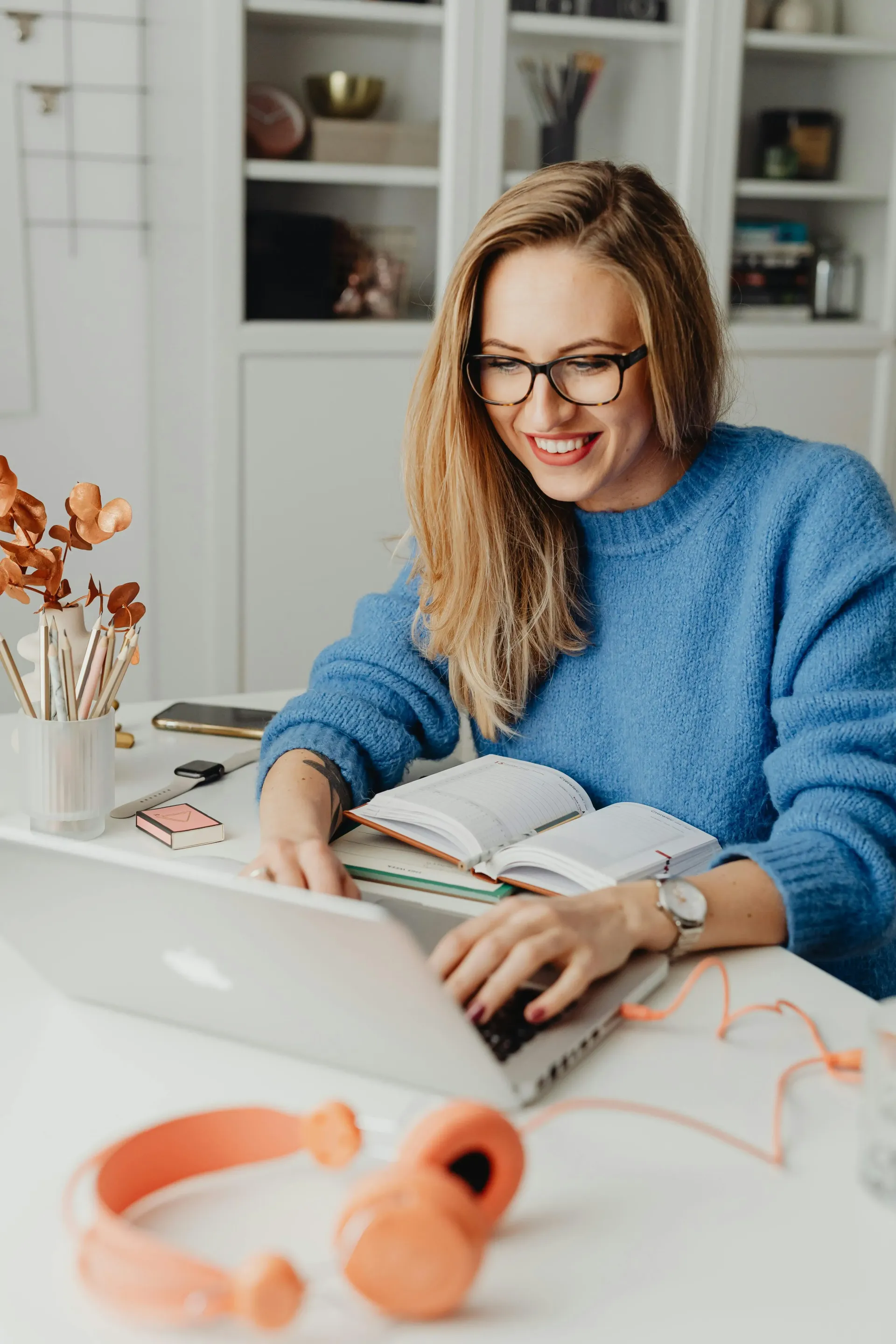 A women with specs, sitting in front of laptop with a open diary.
