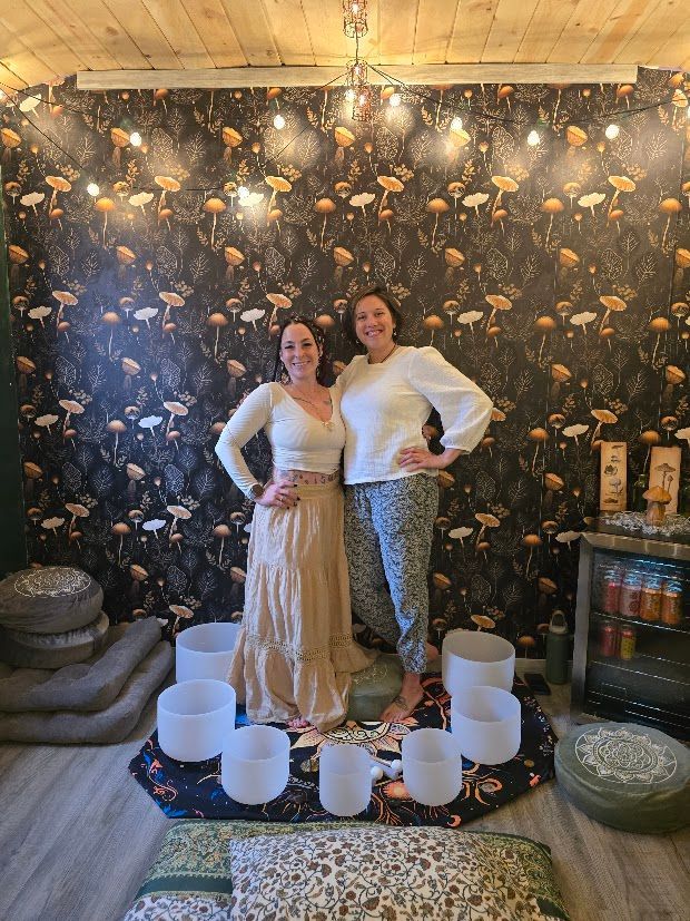 two women standing in front of a mushroom wall with crystal sound bowls around them
