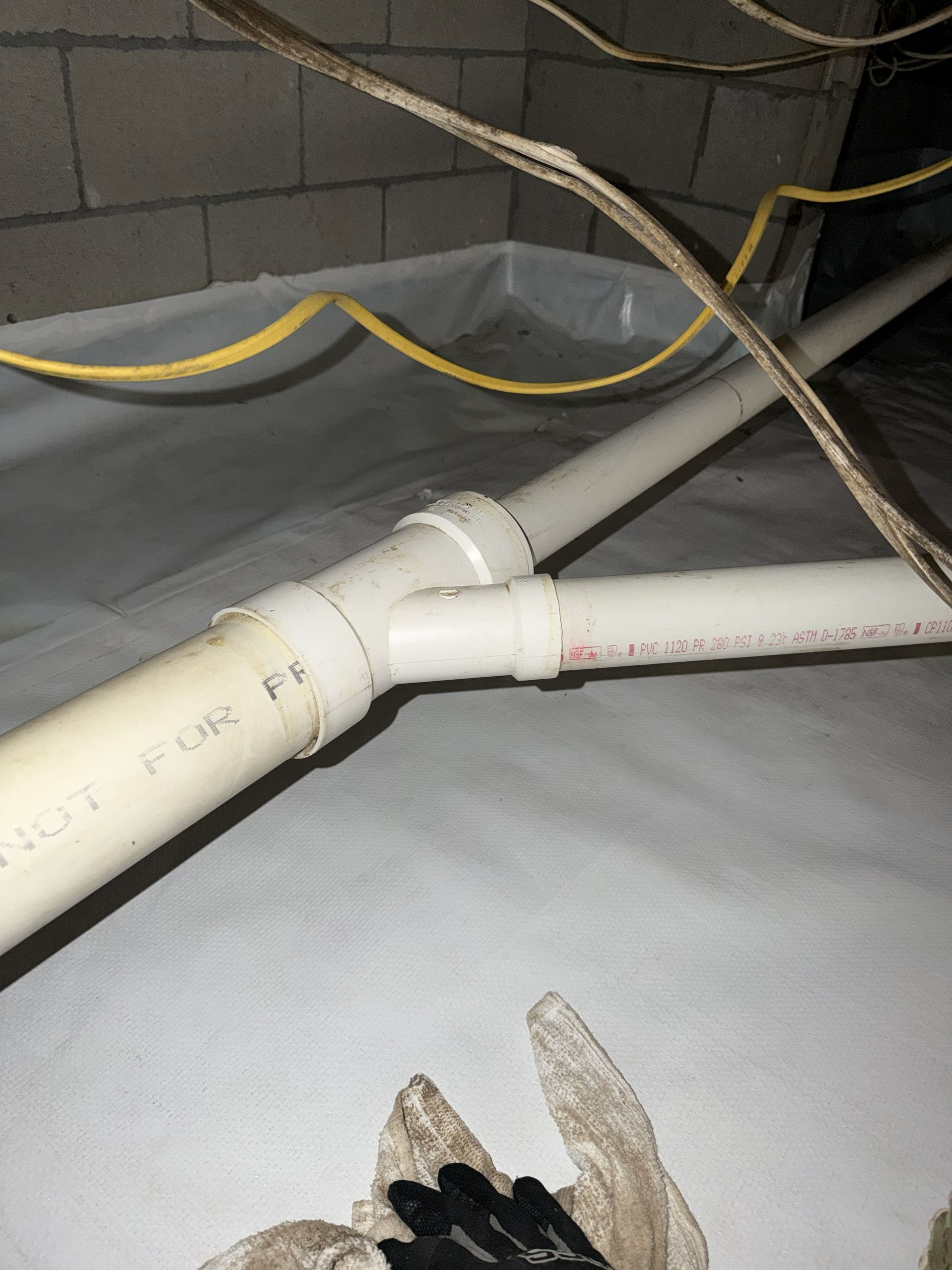Hands installing a silver flexible dryer vent hose behind a dryer near a wall.