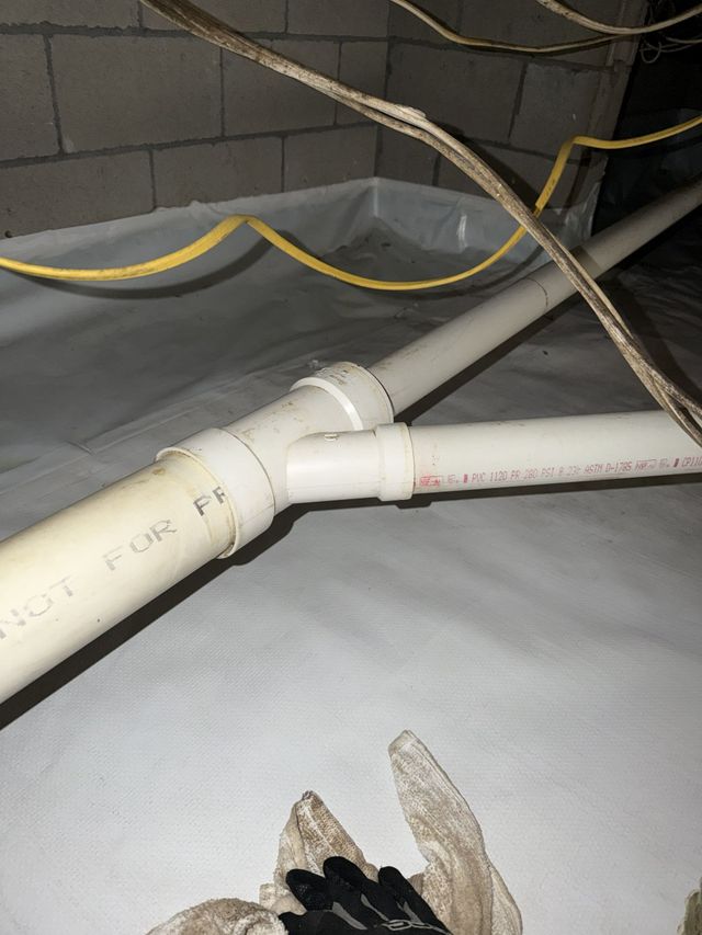 Hands installing a silver flexible dryer vent hose behind a dryer near a wall.