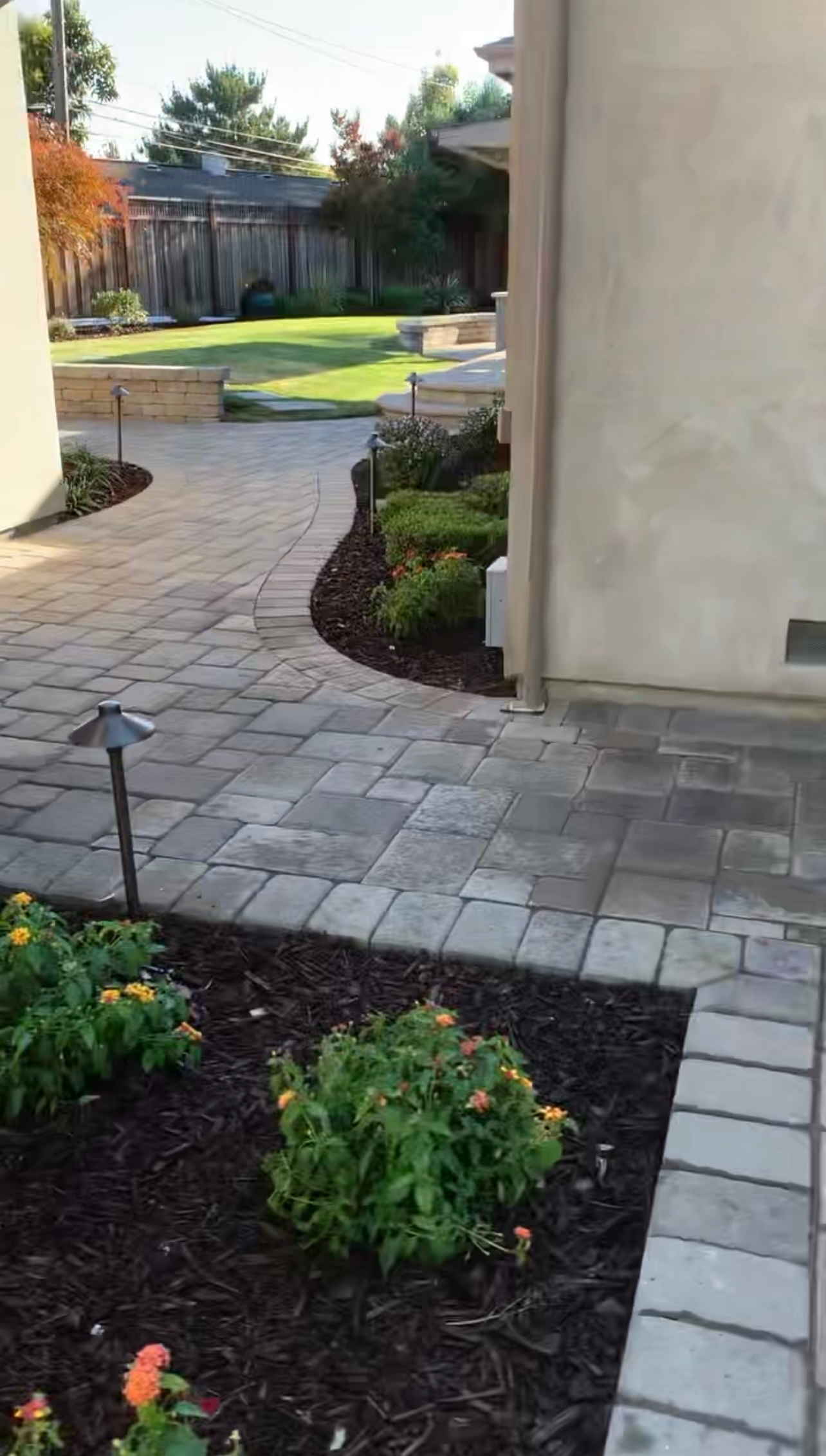 Stone pathway curves through a landscaped yard with green shrubs, leading to a lawn.