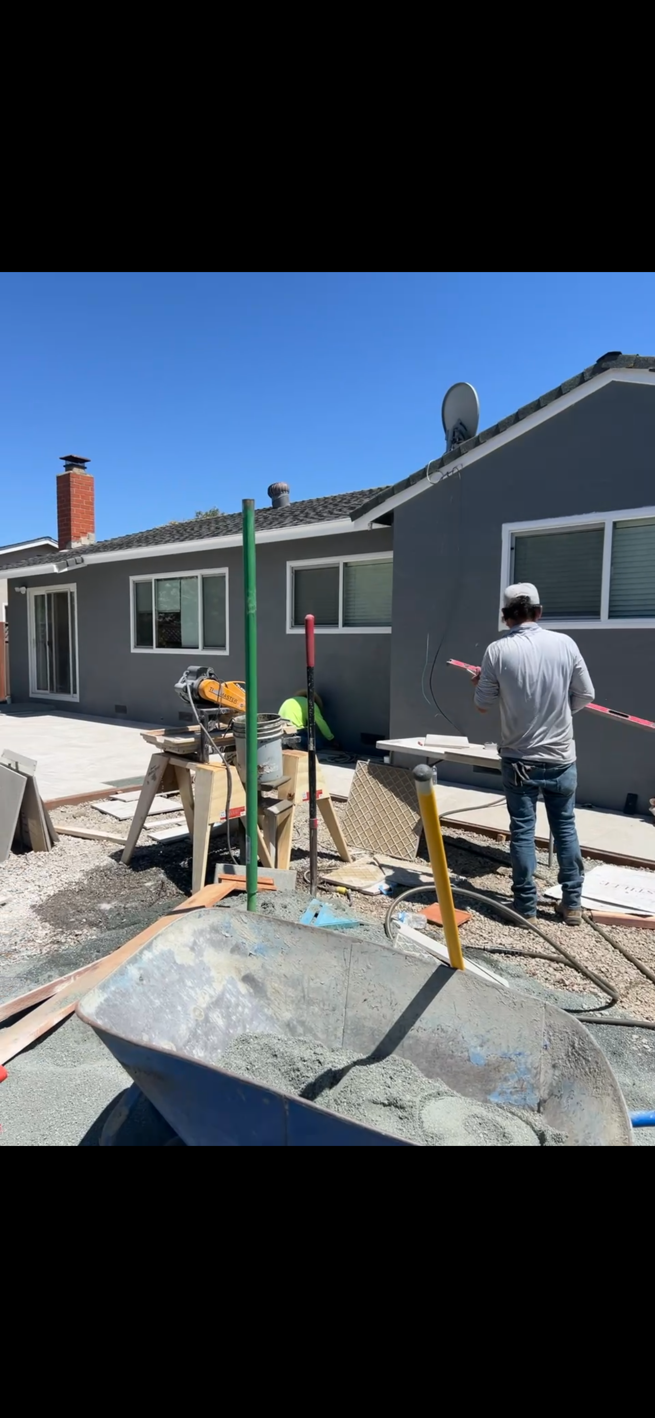 Paved driveway leading to a cream-colored house, framed by palm trees and lush green landscaping.