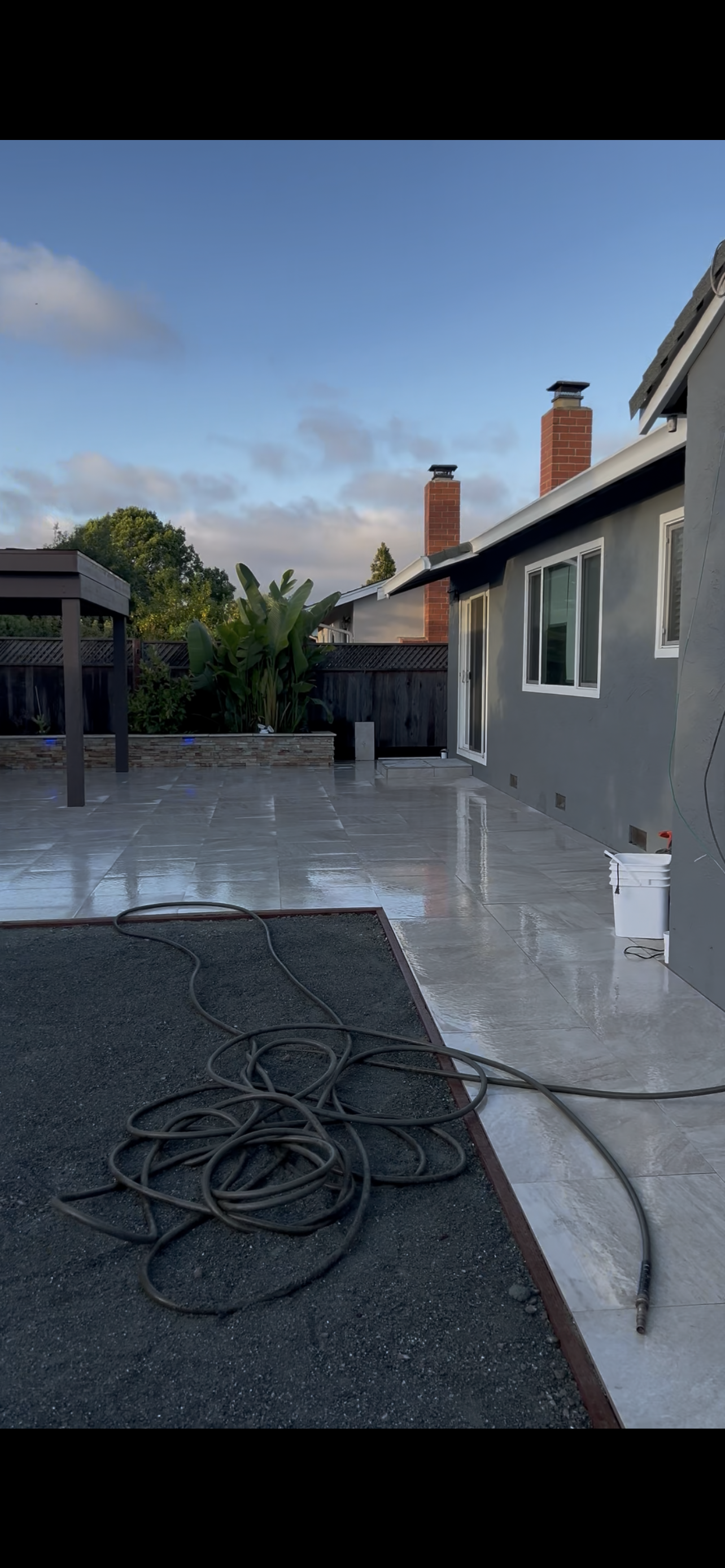 A wet patio with a hose, a house, and a cloudy sky.