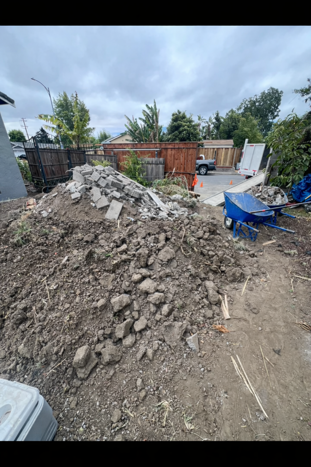 Pile of dirt and debris in a yard; a truck is in the background, cloudy sky.