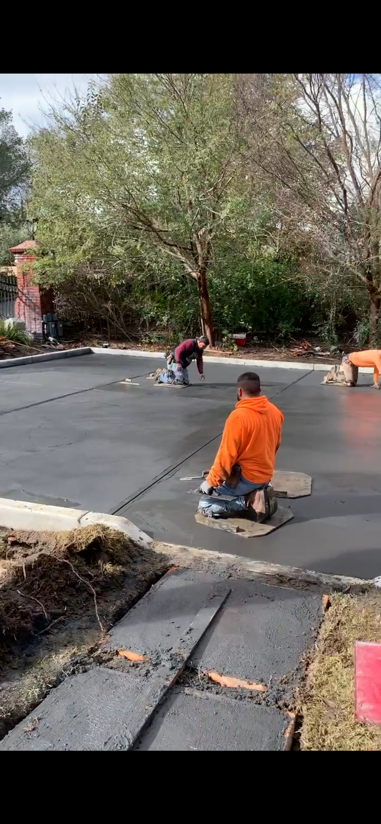 Construction workers smoothing fresh concrete outdoors. One kneels, others work in the background.