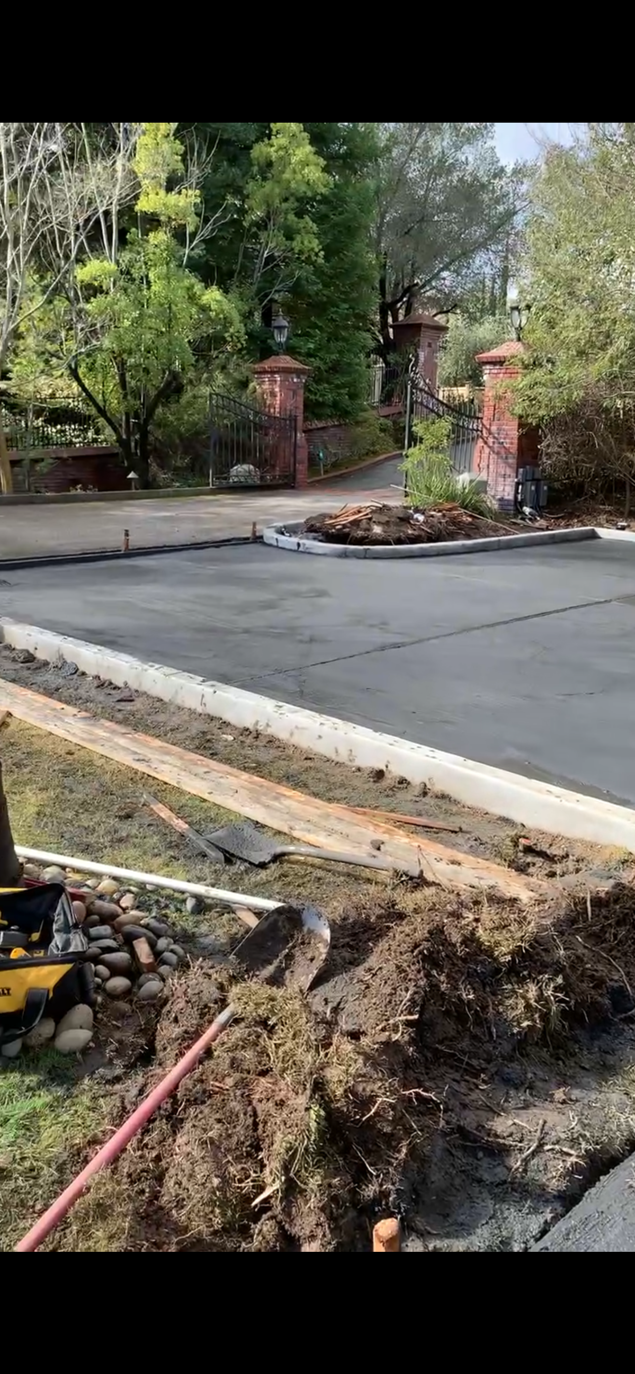 Road construction site with dirt, asphalt, and trees. Entrance gate in the background.