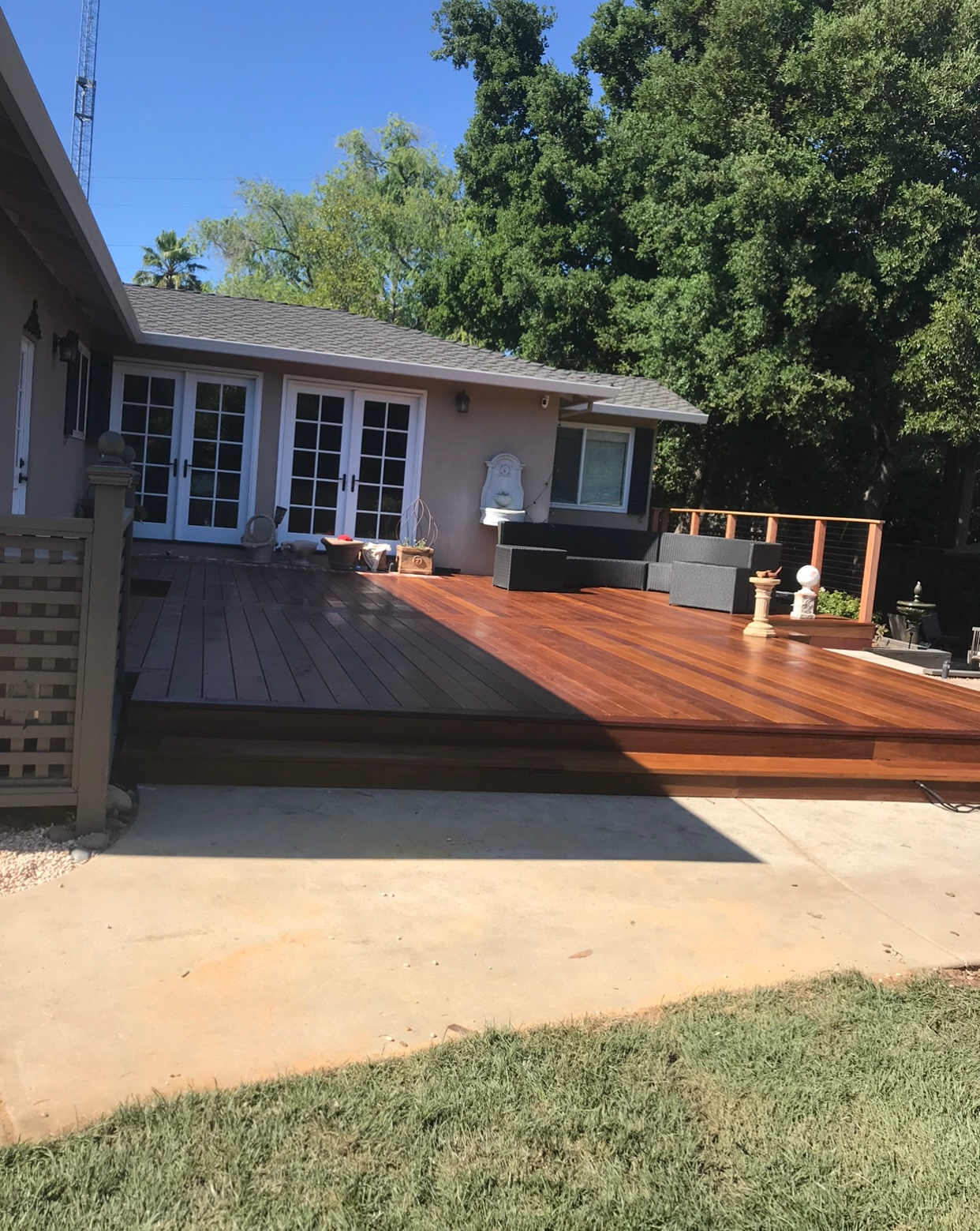 Wooden deck with French doors leading to a house. Sunny day with trees in the background.