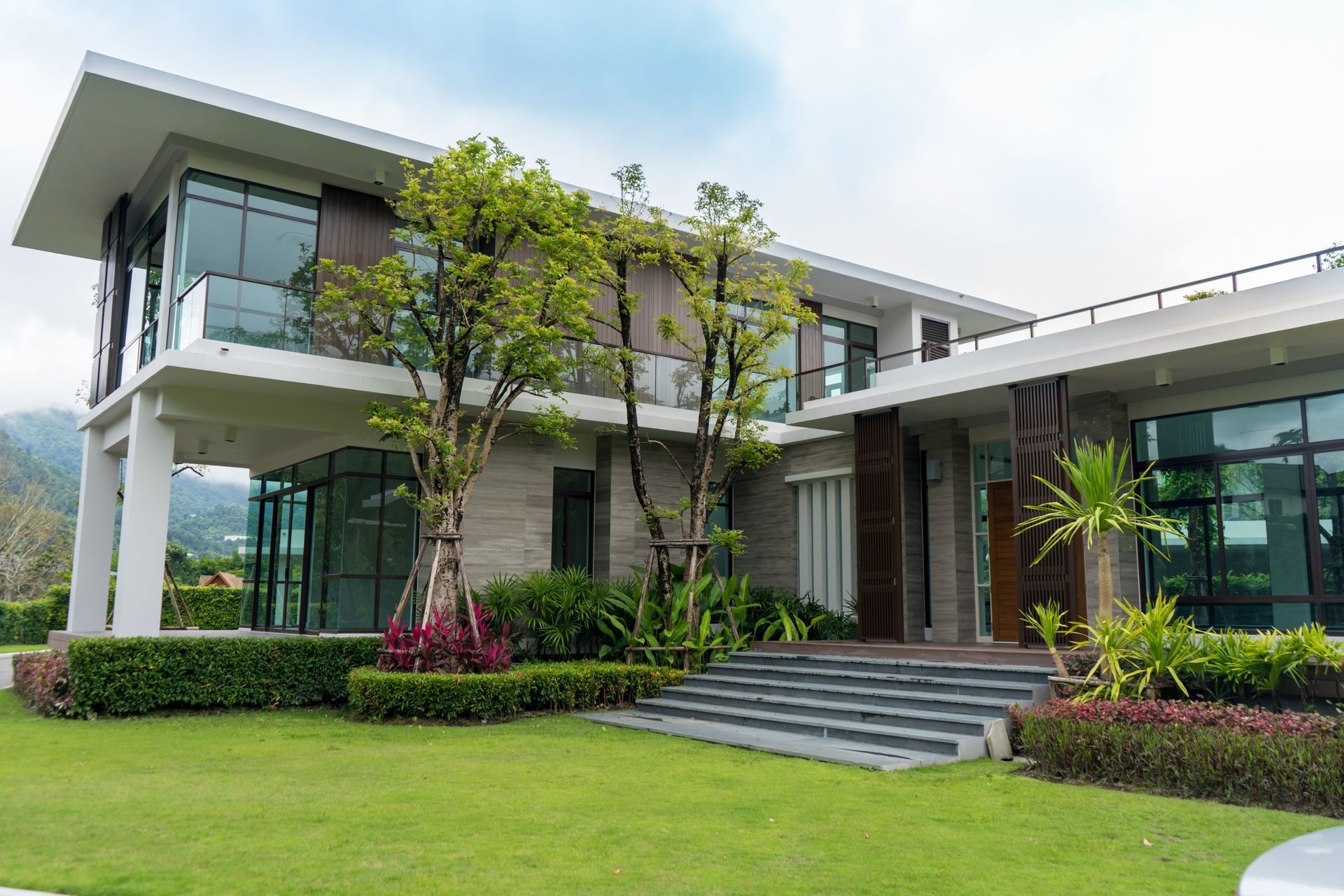 Modern two-story house with large windows, surrounded by green lawn and landscaping.