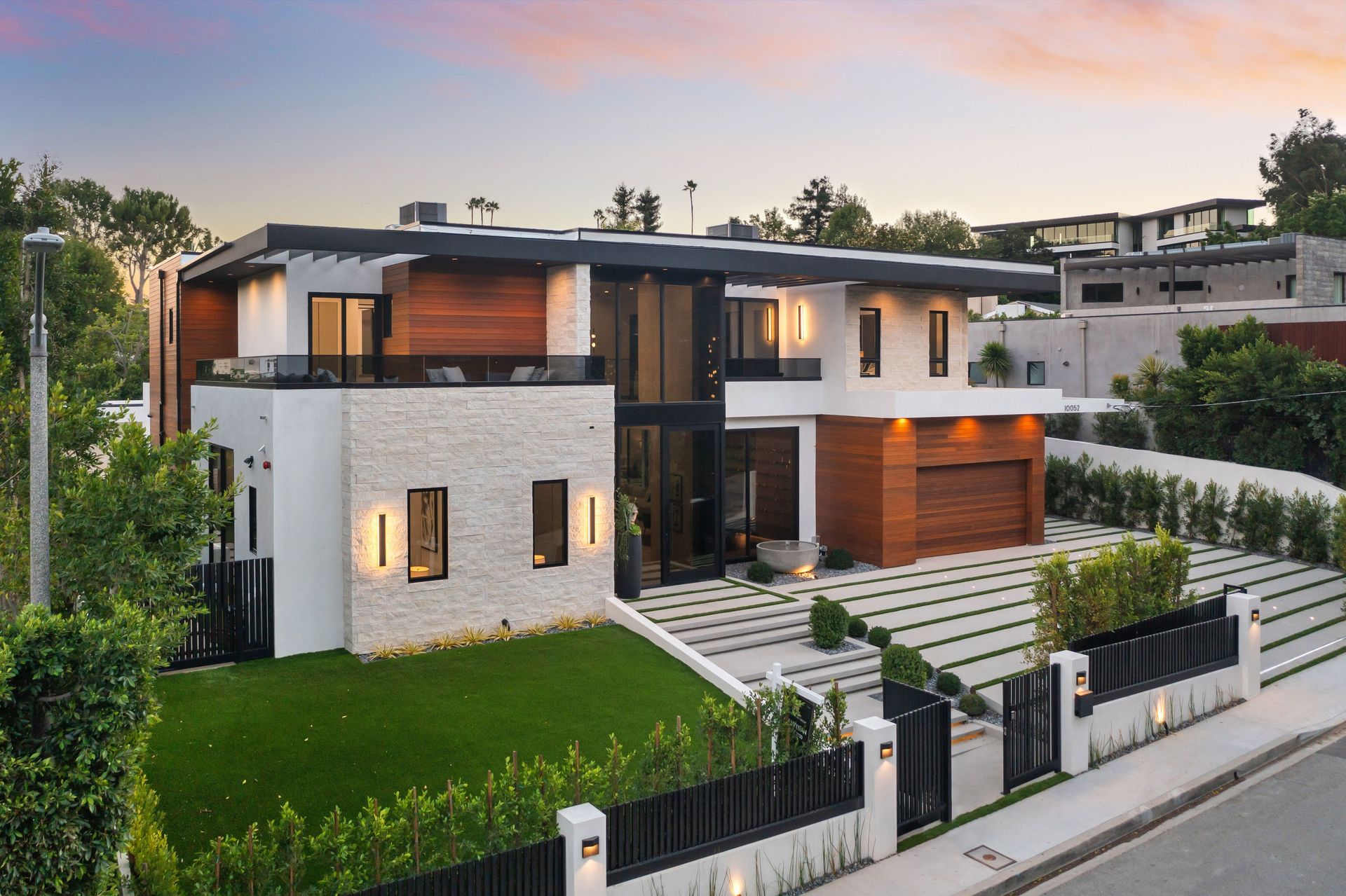 Modern two-story house with white walls, wood accents, and a stone facade, on a green lawn with a driveway.