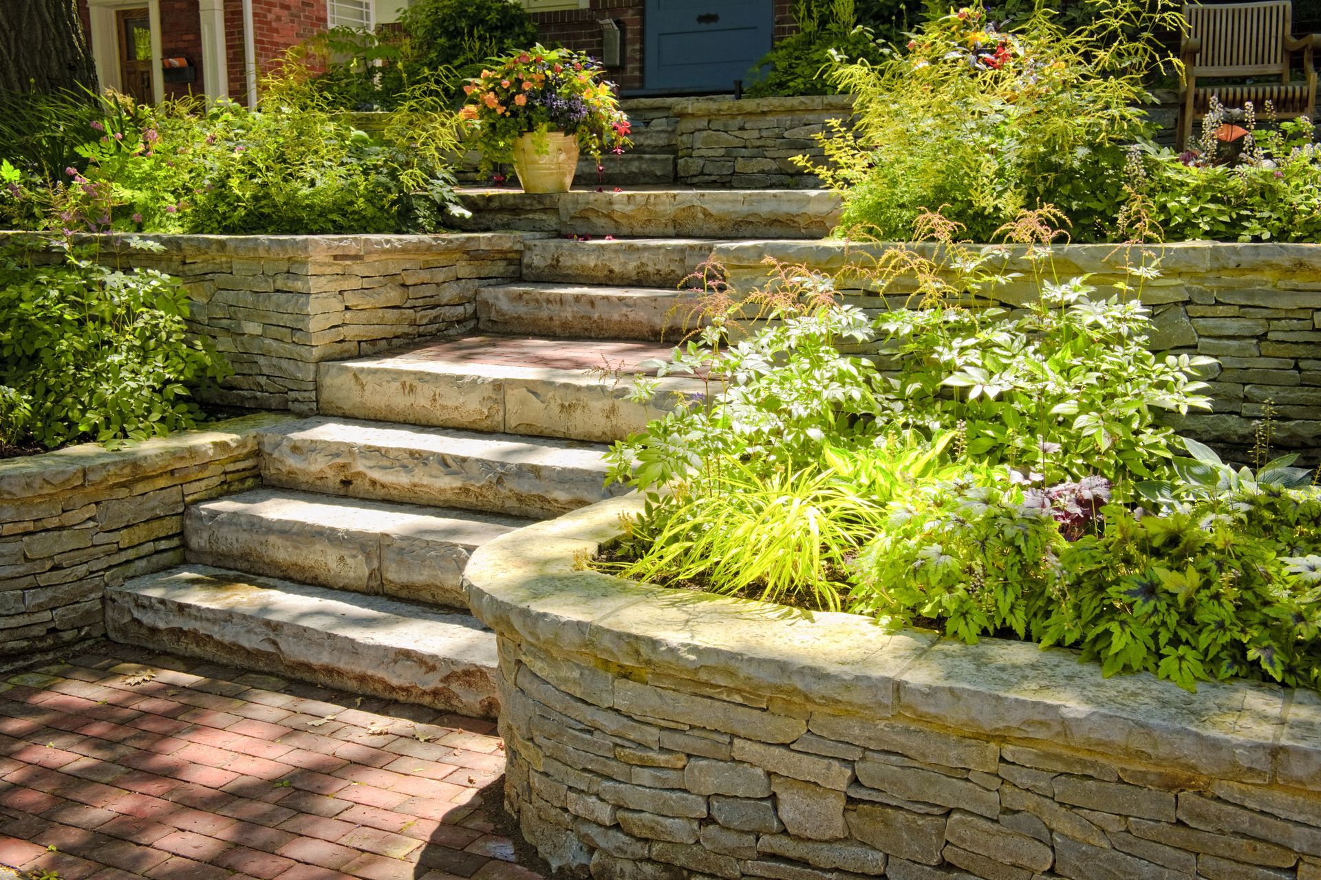 Stone steps with flowerbeds and lush greenery leading to a blue door.