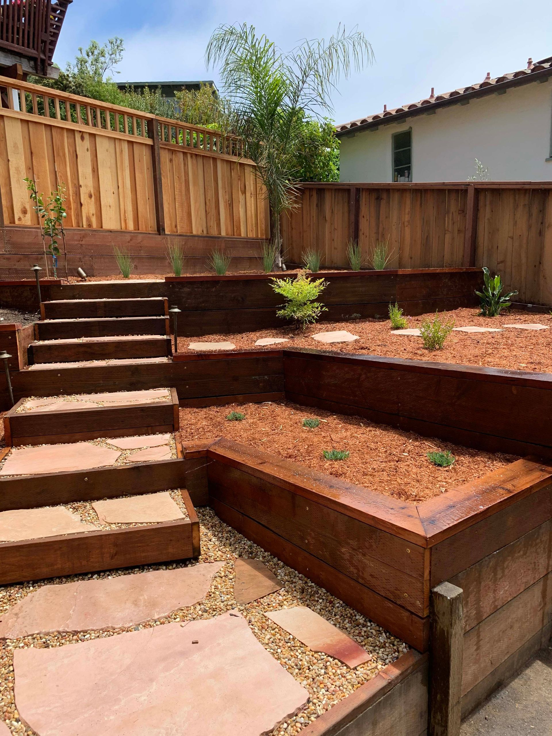 Wooden planter box overflowing with green plants and white flowers, outdoors.