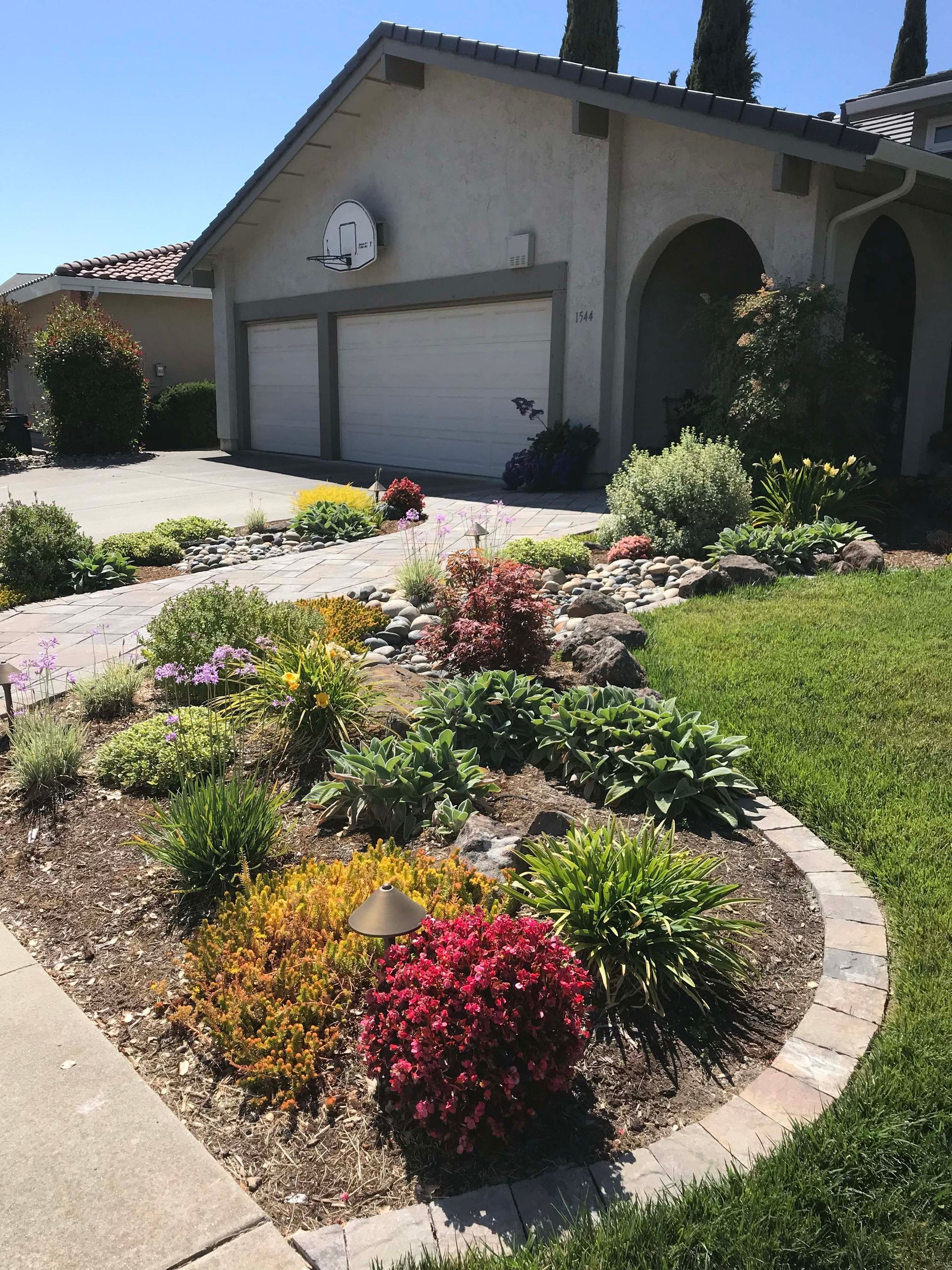 Colorful front yard garden bed with pathway leading to a house with a basketball hoop over the garage.