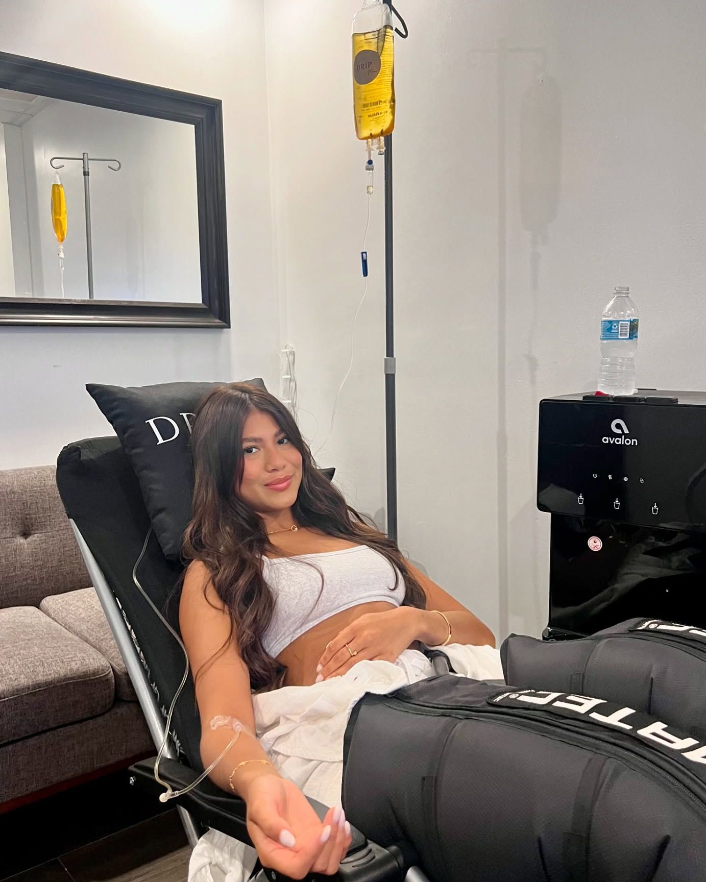 Woman receiving IV treatment, reclining in chair, with leg compression devices. Bright interior.
