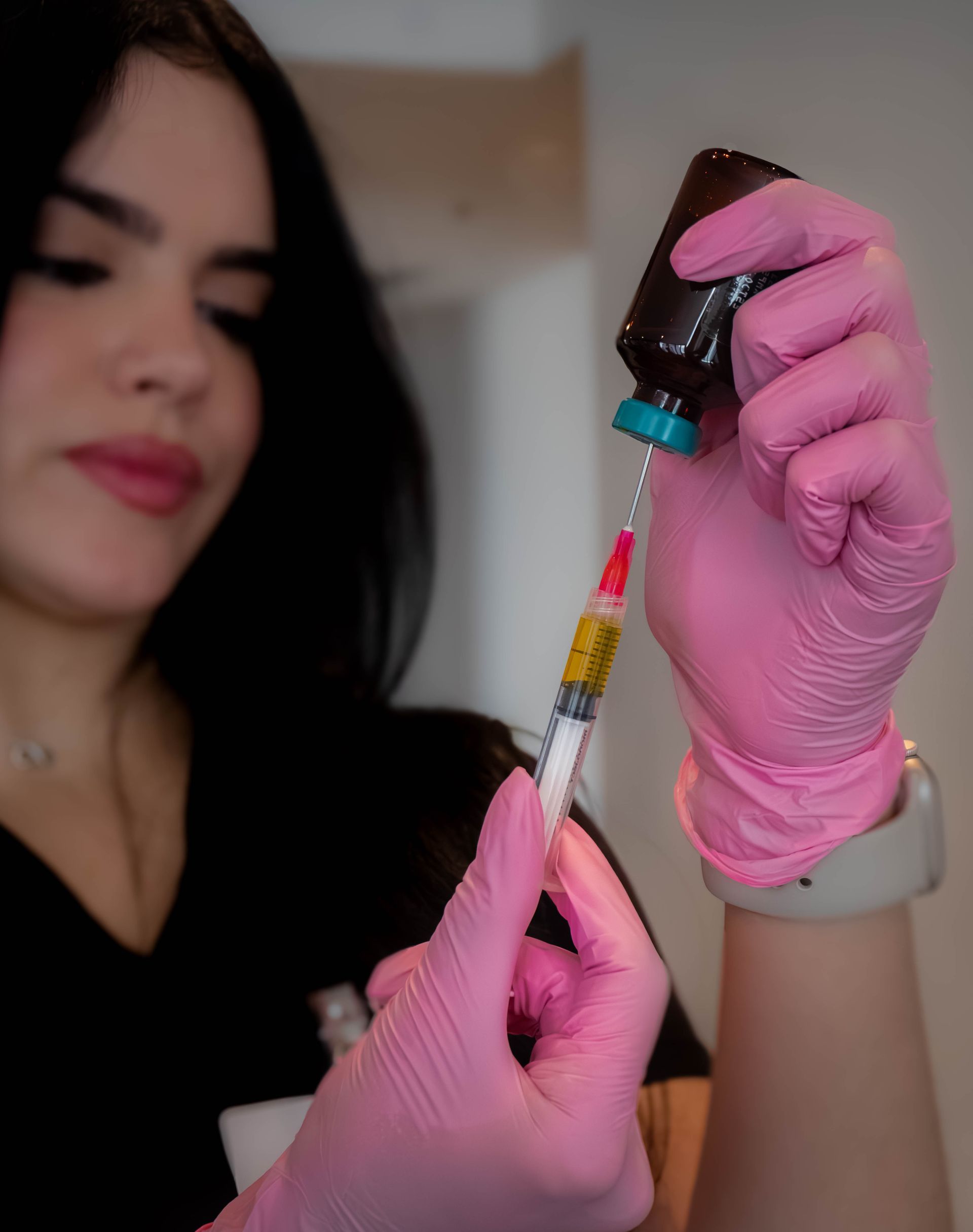 Woman in pink gloves filling a syringe from a brown vial, likely administering an injection.
