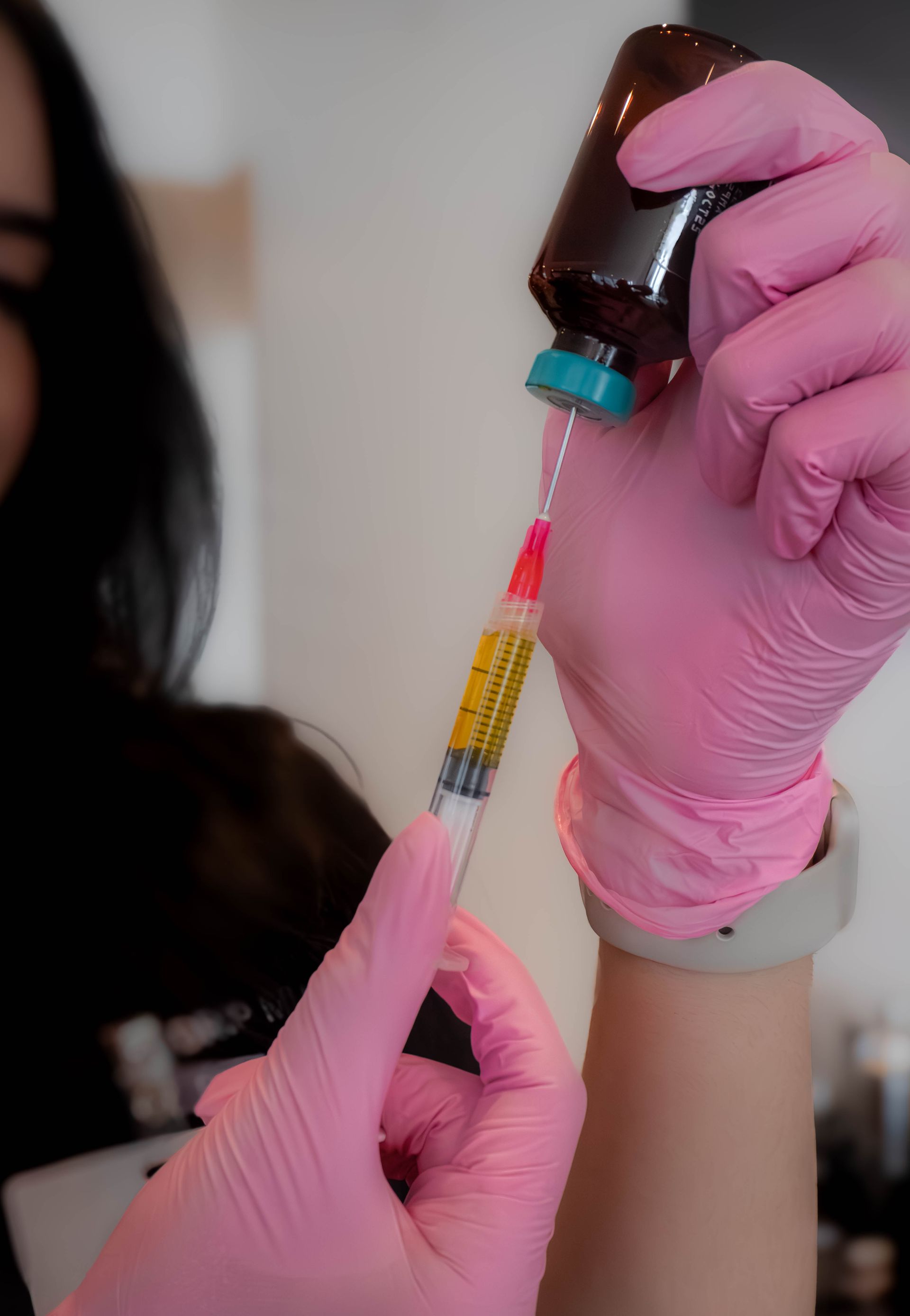 Person in pink gloves filling a syringe with a yellow liquid from a brown bottle.