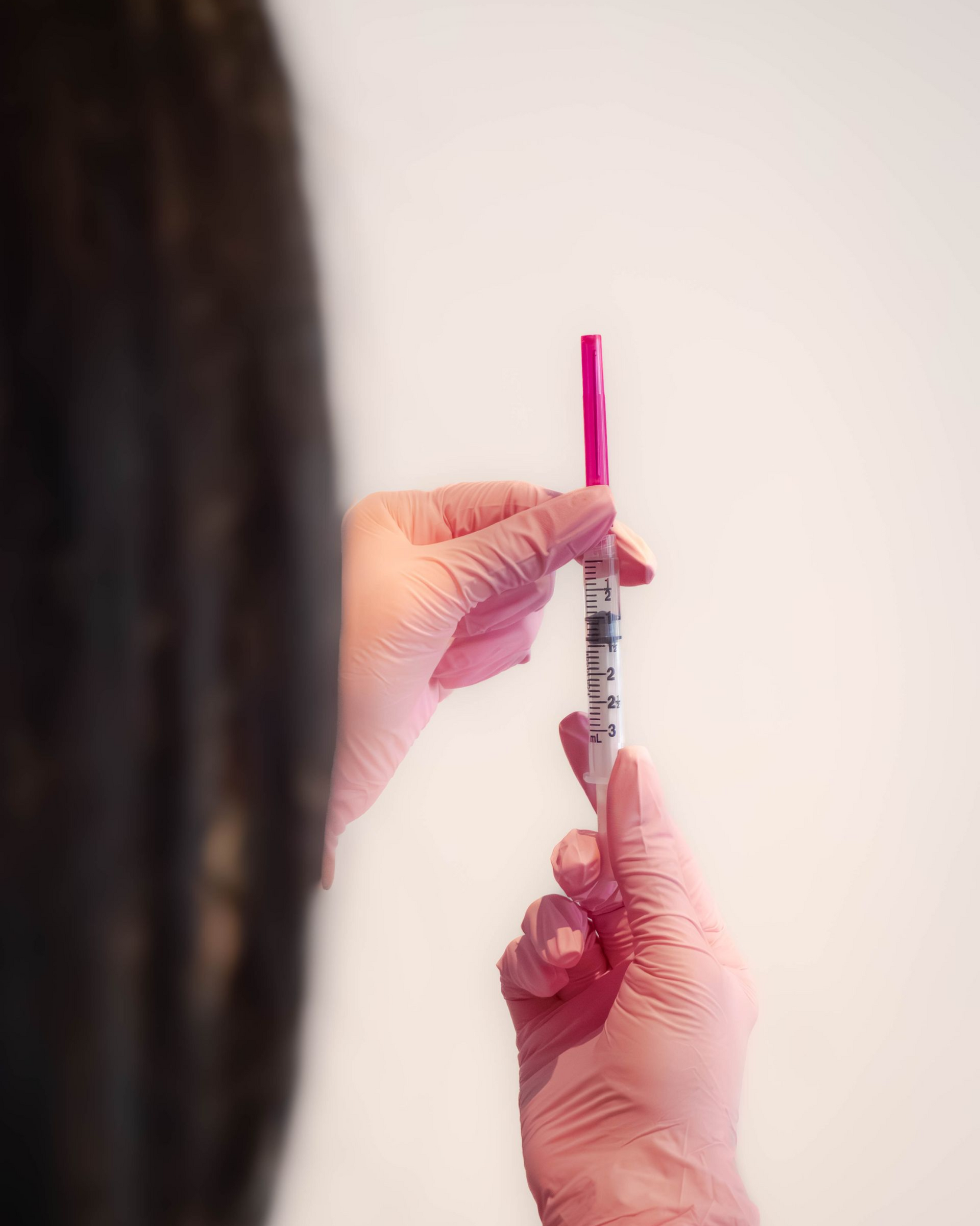 Person in pink gloves holding syringe with a pink plunger.