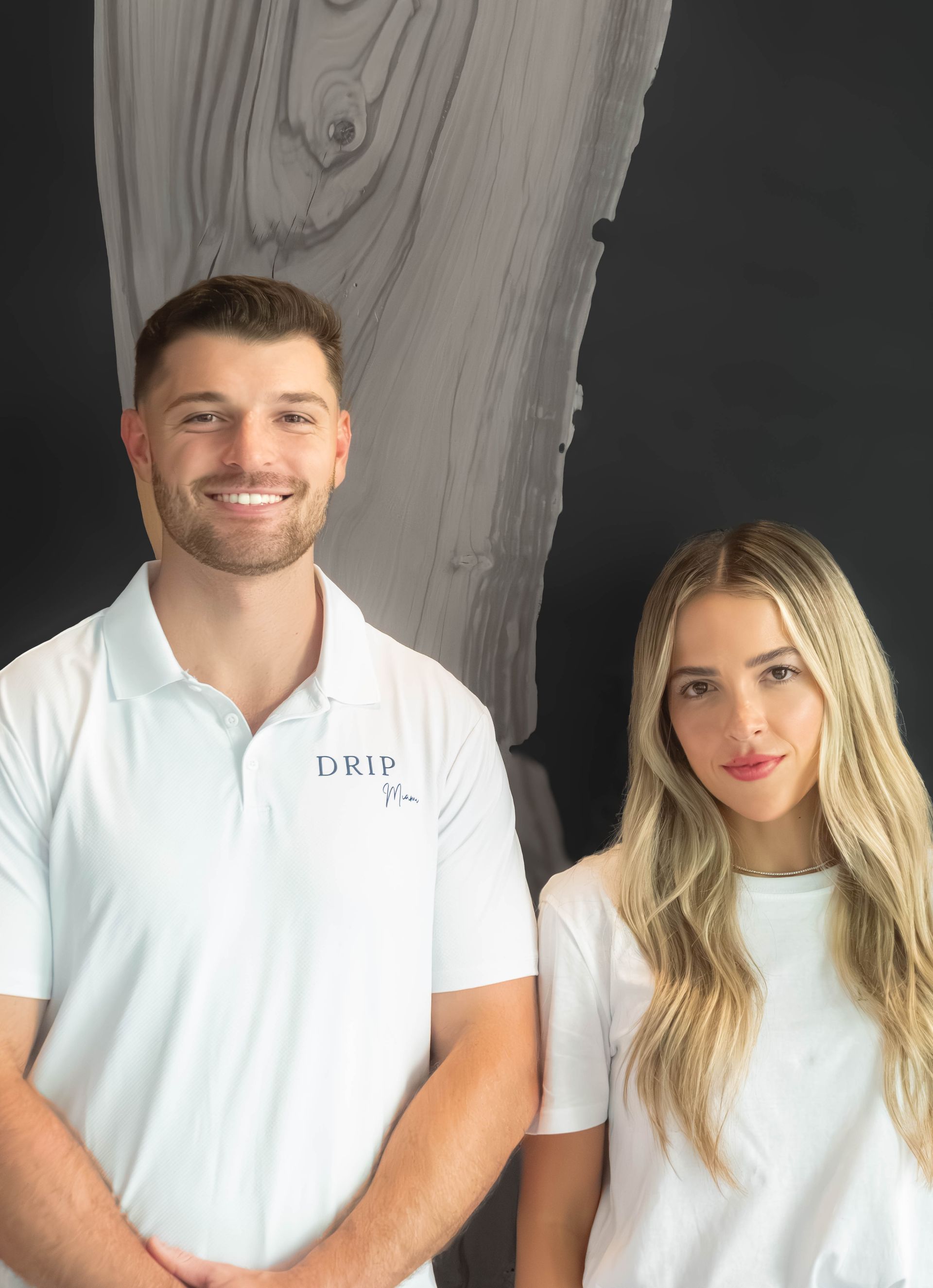 Man and woman in white shirts smiling, standing against a black and wood-grain wall.