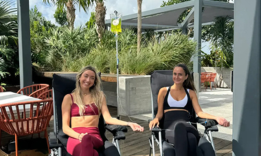 Two women receive IV drips outdoors, smiling.