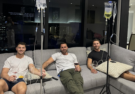 Three men receiving IV drips while relaxing on a couch.