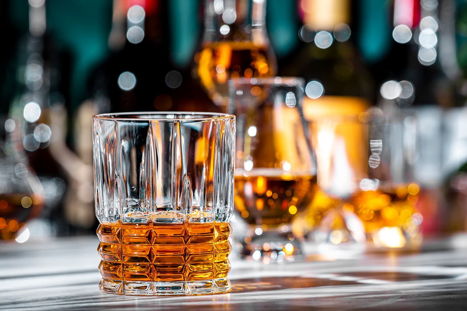 Whiskey glasses with amber liquor on a bar counter, with blurred bottles in the background