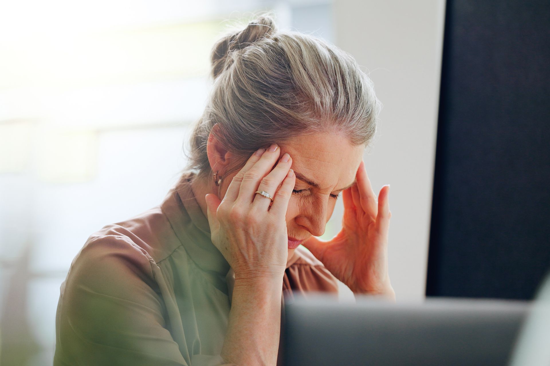 A person sitting at a computer with their hands pressed against their temples, appearing stressed or having a headache.