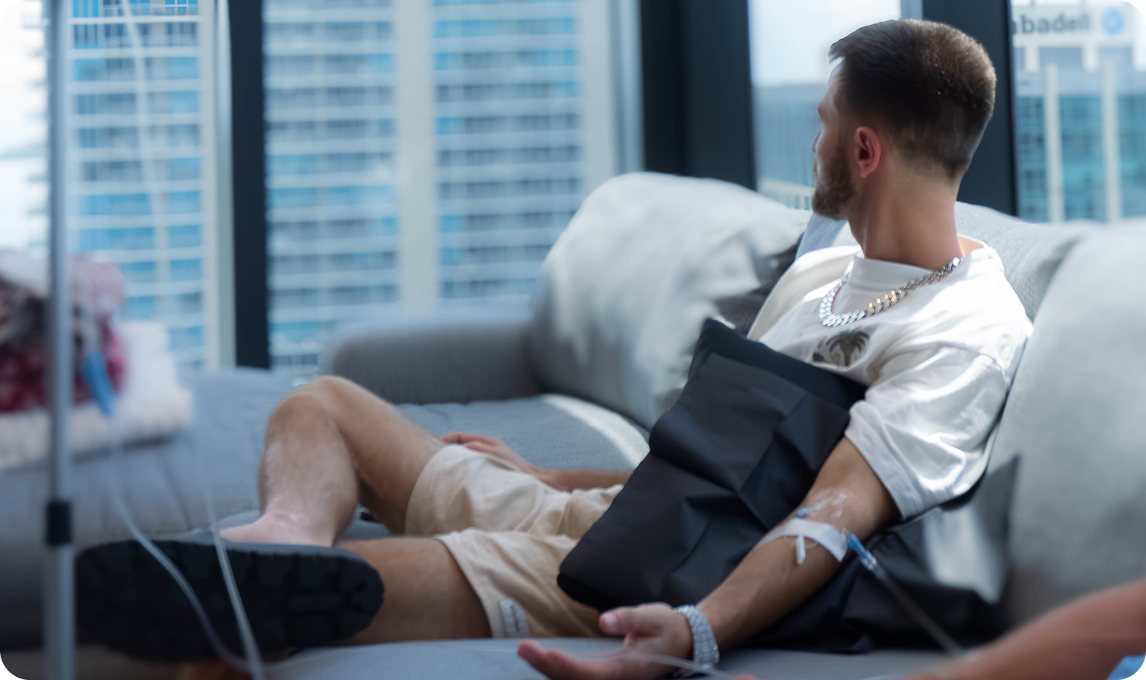 Man on a couch receiving IV fluids in a modern room with city view.