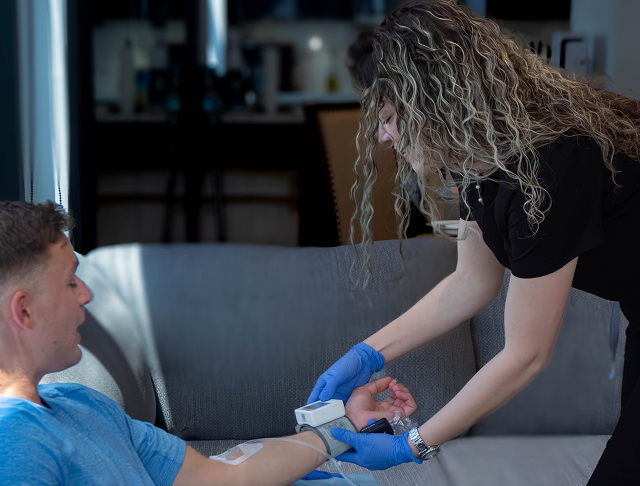 Woman receiving IV drip, smiling, in a medical spa setting. Black recliner, water dispenser visible.