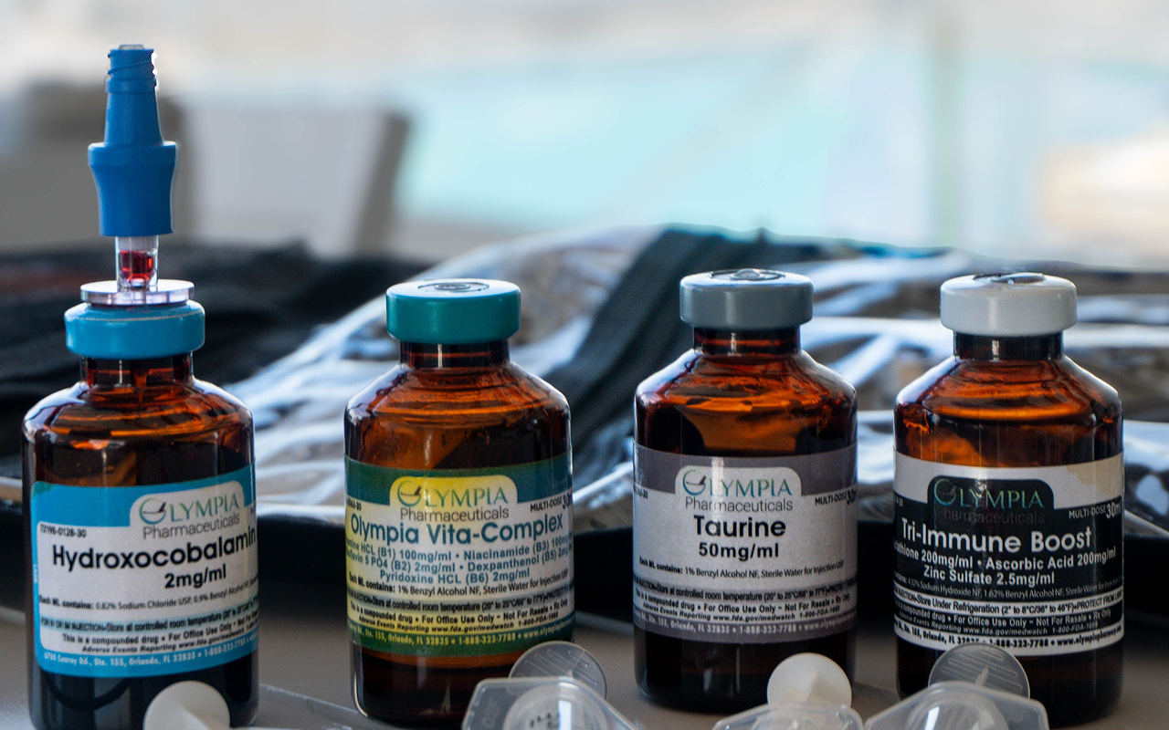Four medicine vials with labels and a syringe are on a table.