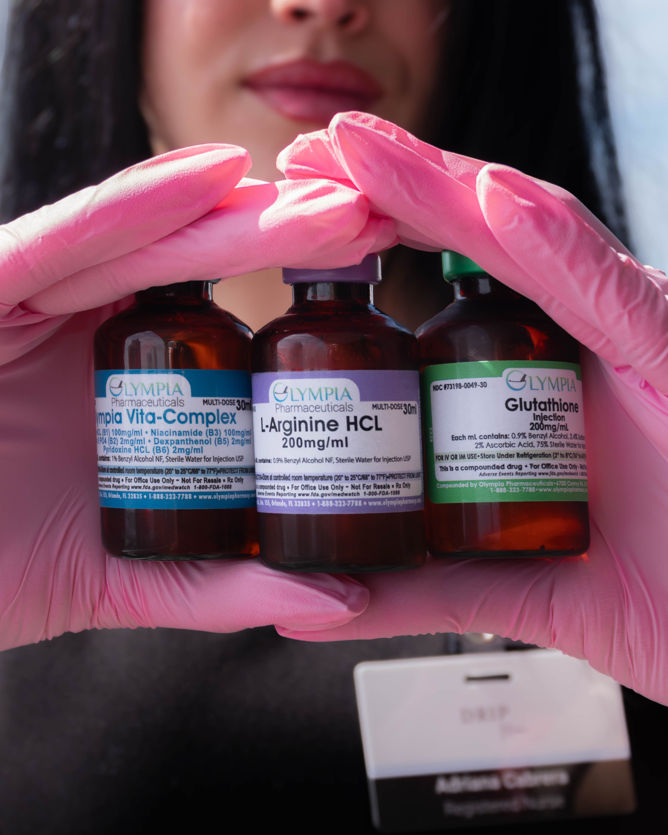 Woman in pink gloves holding three vials labeled with medical terms.