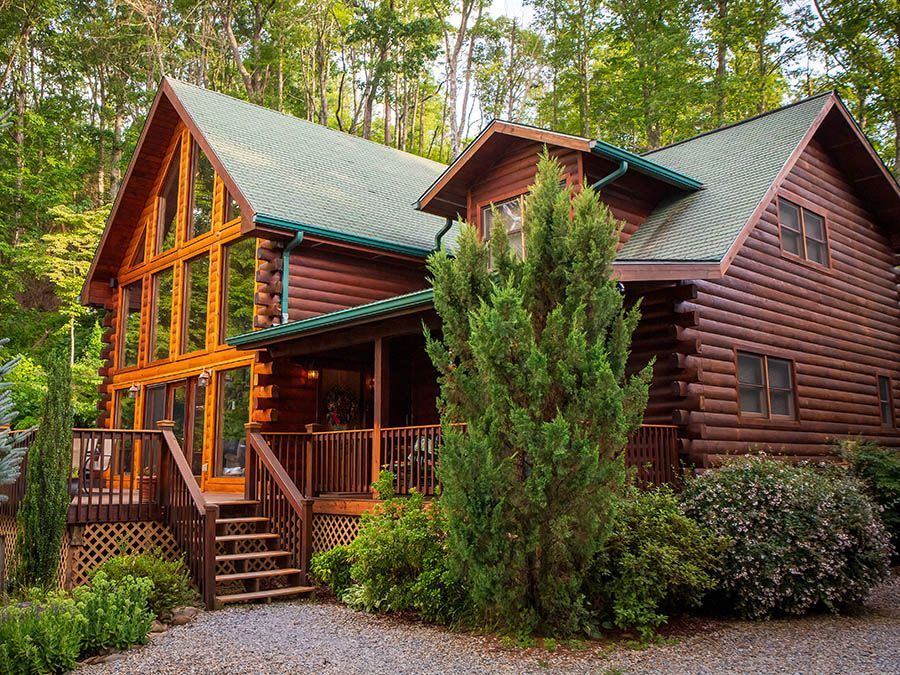 A large log cabin with a green roof is surrounded by trees.