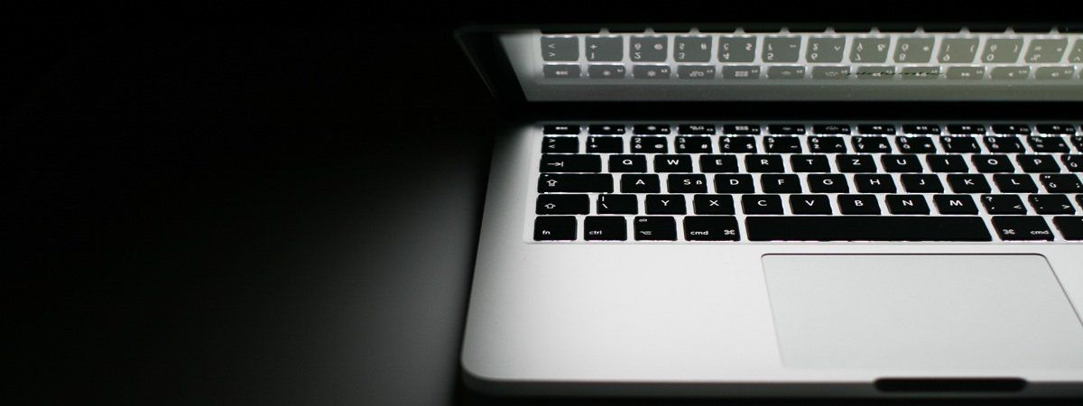 A laptop computer is open and sitting on a table in the dark.
